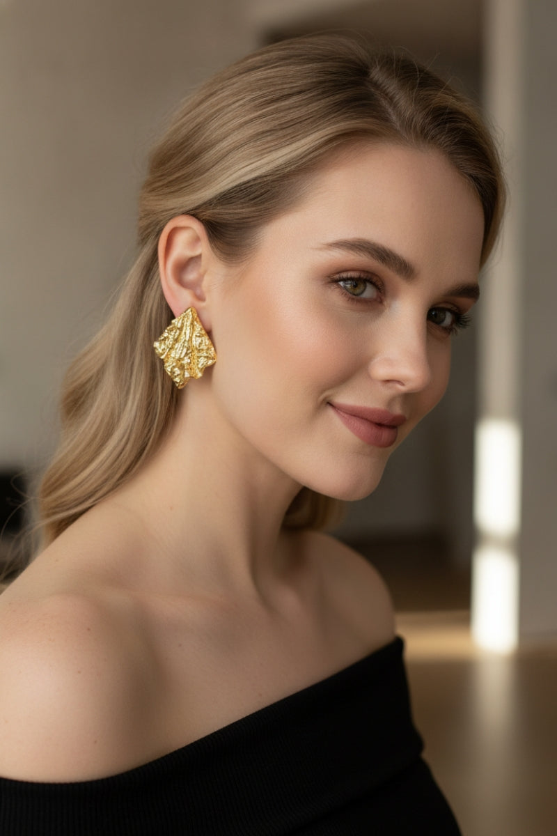 A portrait capturing the artisanal sculptural aesthetic of the gold Mirage Earrings, worn with a stylish off-shoulder top.