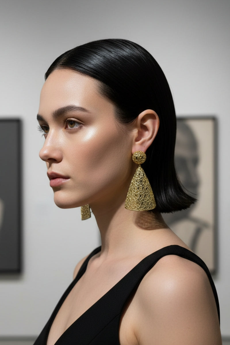 Sophisticated woman at a contemporary art gallery wearing hollow geometric gold cone earrings, minimalist chic aesthetic.