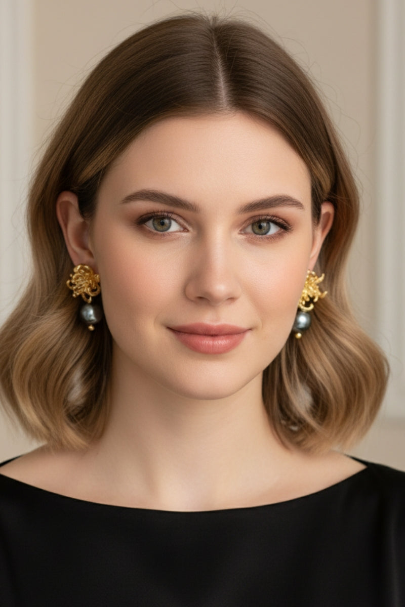 Front view portrait of a woman wearing a matching pair of nickel-free statement drops featuring detailed gold chrysanthemum floral bases and symmetrical tahitian-style black pearls, ideal for timeless formal styling.