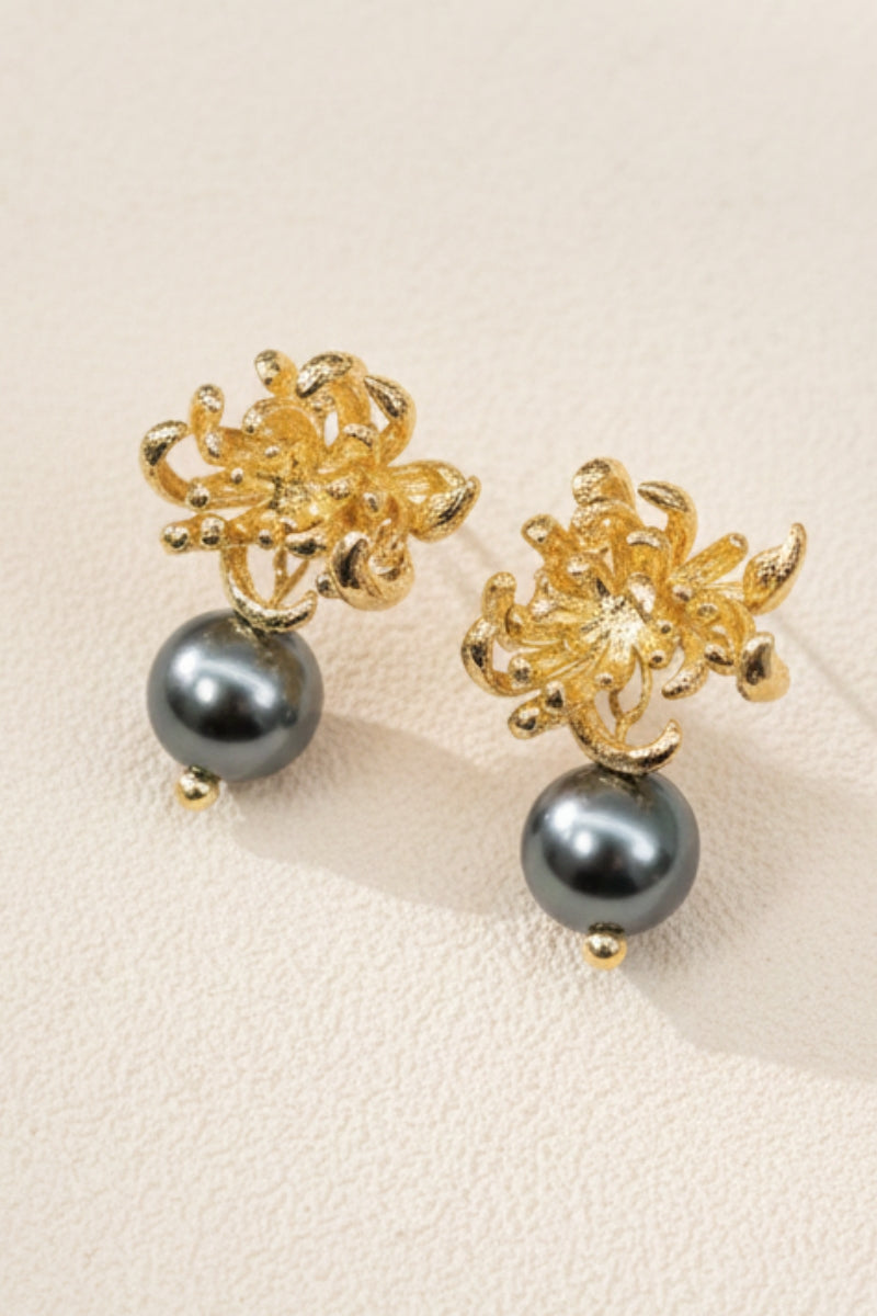 A pair of Obsidian Bloom 18K gold-plated sculptural floral drop earrings with lustrous black pearls on a sand surface, perfect as dark academia aesthetic jewelry or a elegant wedding guest statement accessory.