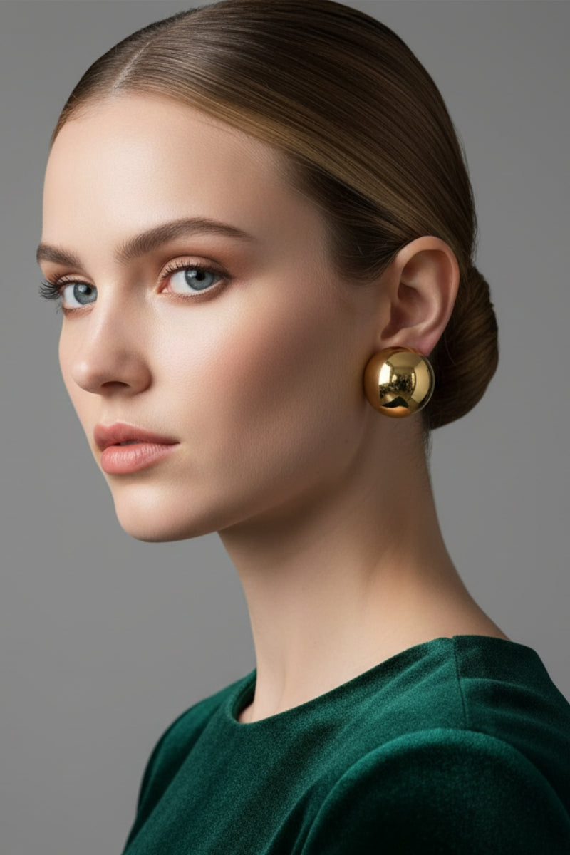 An elegant woman in an emerald green velvet dress accessorized with Aura Sculpted Dome Studs, demonstrating how these premium 18K gold plated chunky sphere earrings add an effortless touch of geometric luxury to evening wear.