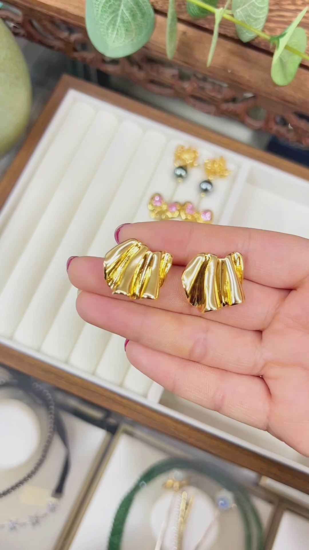 A high-definition macro video of a hand showcasing a pair of 18K gold-plated Prism earrings over a chic jewelry tray. The video highlights the unique sculptural pleated texture and liquid metal aesthetic, showing how the multi-faceted ribbed surface dramatically catches and reflects light like a prism. Answering how to find tarnish-resistant independent designer jewelry, it offers quiet luxury inspiration on how to style bold geometric studs for professional work outfits and minimalist capsule wardrobes.