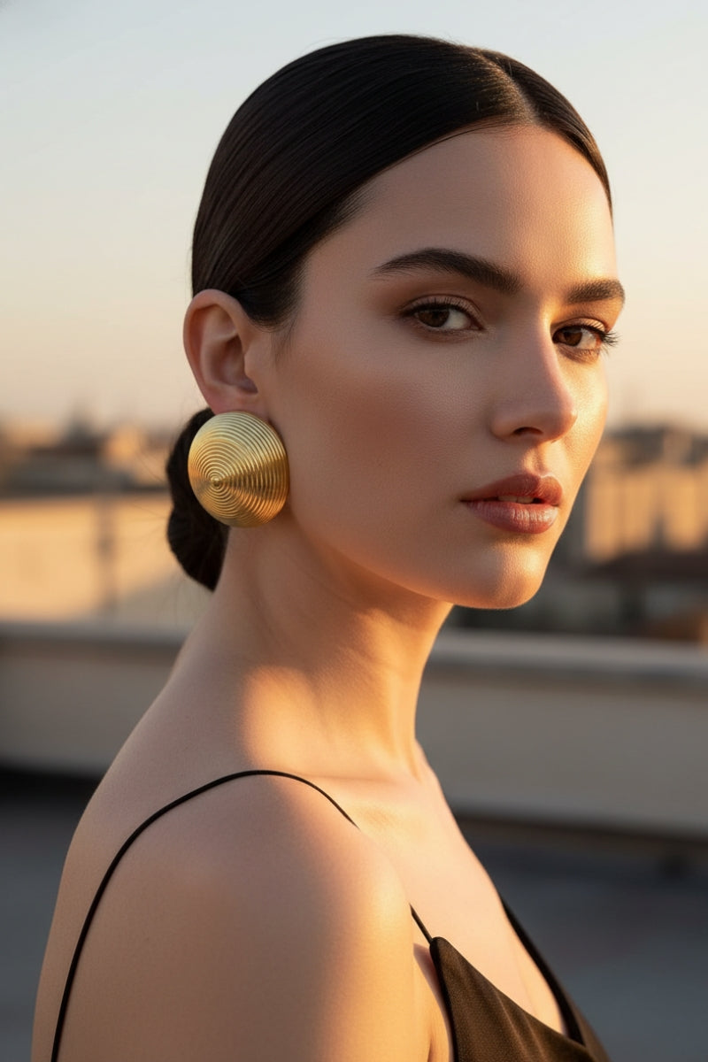 Elegant woman wearing chunky gold ribbed dome earrings with a sleek bun at golden hour, showcasing the 80s retro statement jewelry trend for New York fashion lovers.