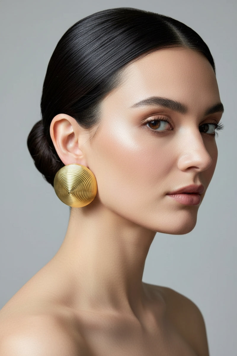 High-fashion editorial shot of sculptural gold concentric circle earrings on a model with neutral makeup, highlighting the bold metal jewelry trend popular in London galleries.