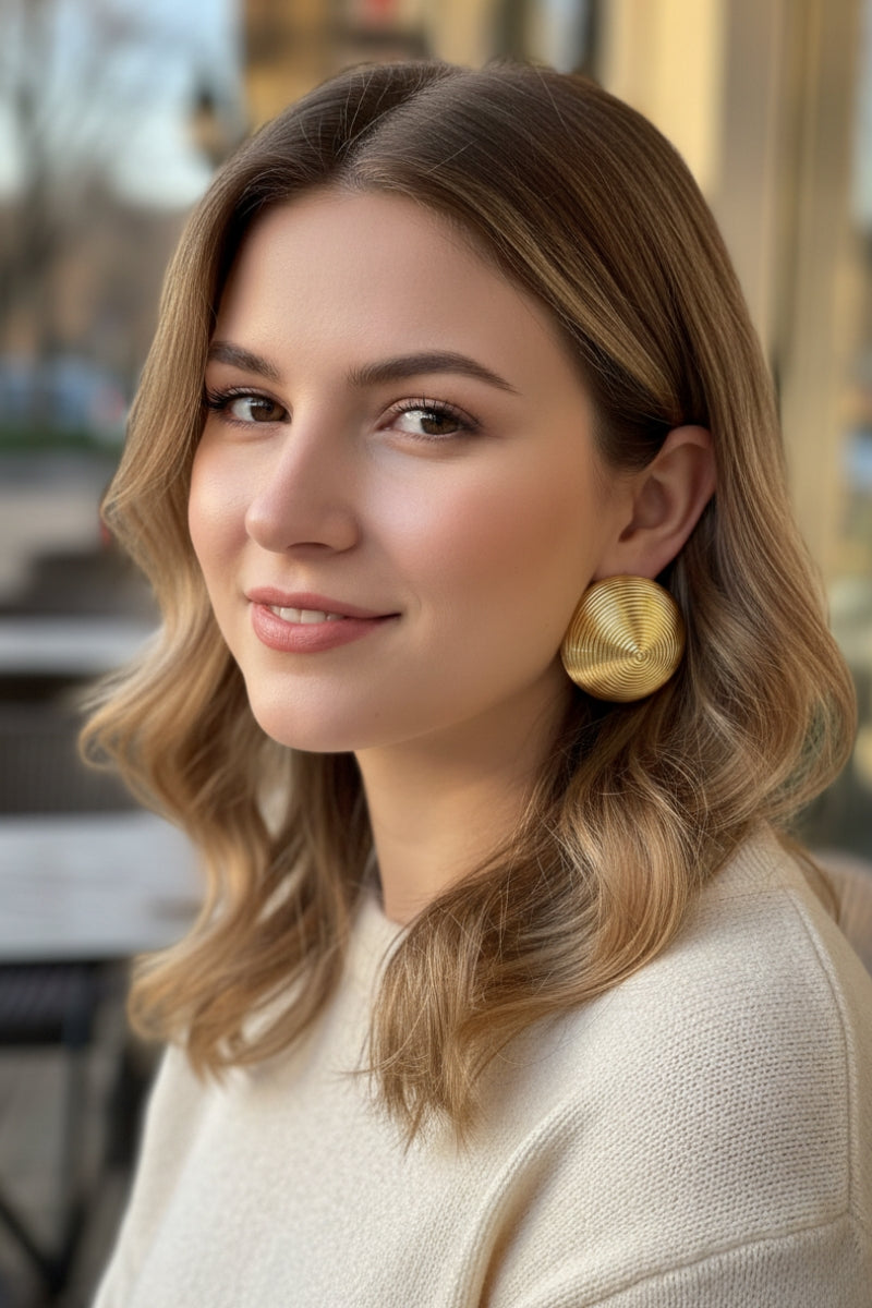 Close-up of a model wearing Juno concentric circle gold dome studs with a beige knit sweater, perfect for the British "Quiet Luxury" autumn outfit aesthetic.