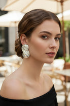 Close-up of a woman with an elegant updo hairstyle wearing Seraphina Sculptural Swirl Earrings in silver. These chunky high-shine earrings feature a distinctive double-spiral design, perfect for sophisticated evening wear.