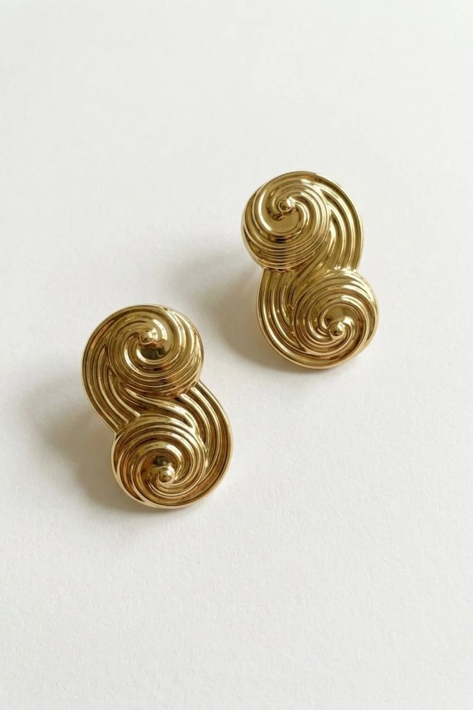 Seraphina Small gold-plated sculptural stud earrings with polished double-swirl detailing, displayed as a pair on a white background.