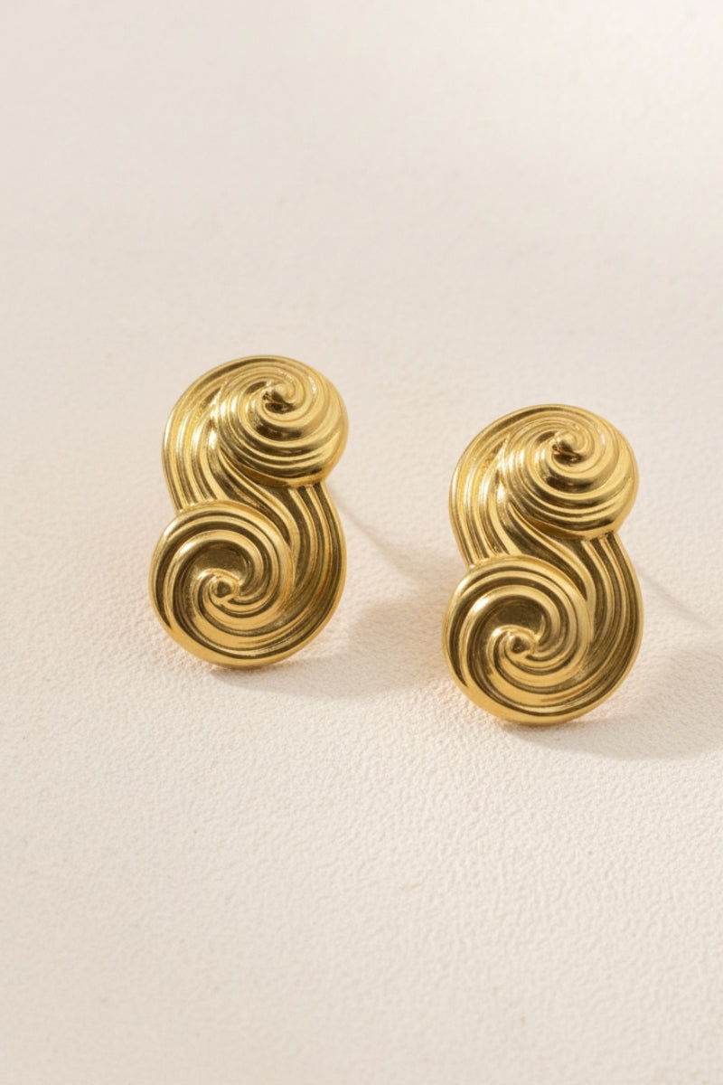 A pair of Seraphina small textured gold S-shape earrings on a neutral background, focusing on the intricate sand-cast finish.