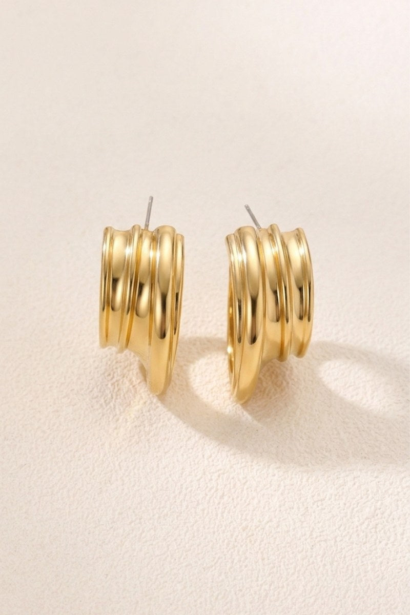 Triple-ribbed wave hoop earrings on a warm beige background