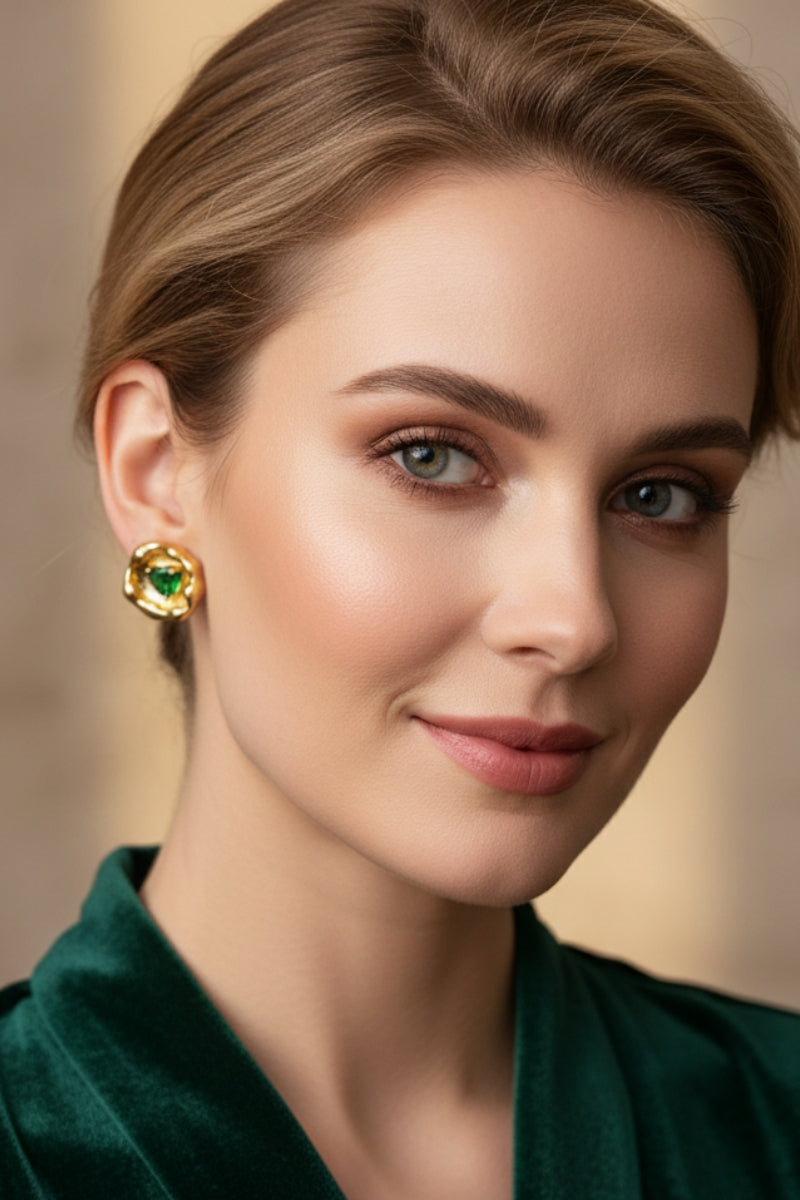 Frontal portrait of a sophisticated woman wearing a liquid-gold textured molten earring with a bright green center stone. Styled beautifully with an emerald green velvet shirt, serving as a unique emerald anniversary jewelry gift idea for her.
