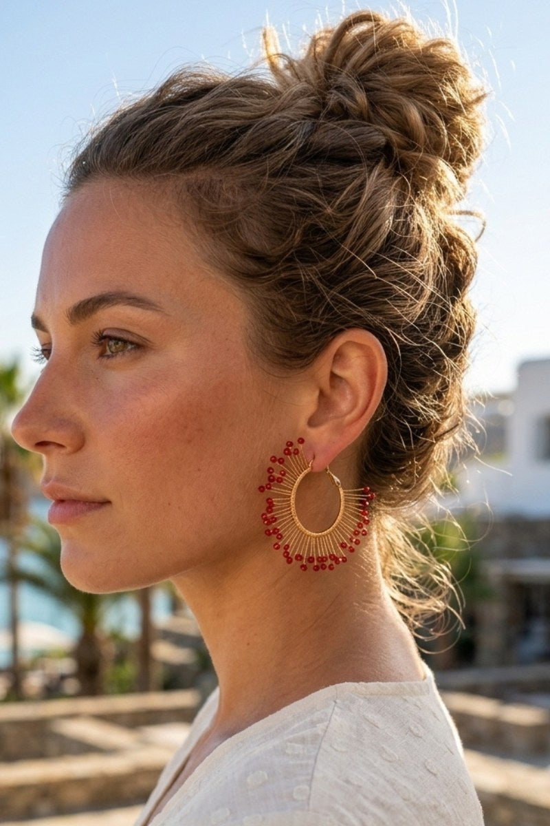 Model wearing solburst wire-wrapped beaded sunburst hoop earrings in the Crimson variant, view 1