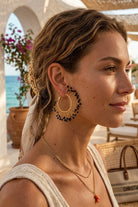 Model wearing solburst wire-wrapped beaded sunburst hoop earrings in the Noir variant, view 1