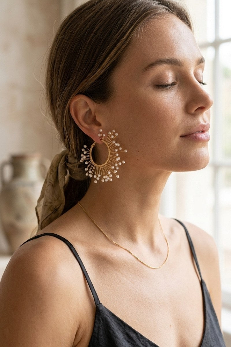 Model wearing solburst wire-wrapped beaded sunburst hoop earrings in the Pearl variant, view 1