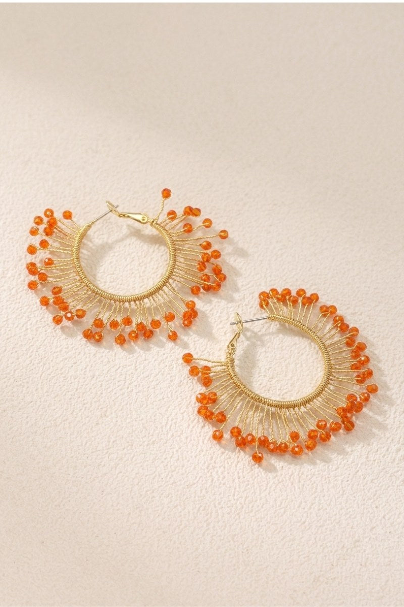 Solburst wire-wrapped beaded sunburst hoop earrings in the Tangerine variant on a warm beige background