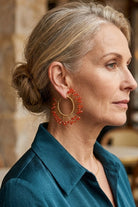 Model wearing solburst wire-wrapped beaded sunburst hoop earrings in the Tangerine variant, view 1